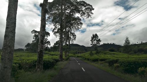 Road amidst field against cloudy sky