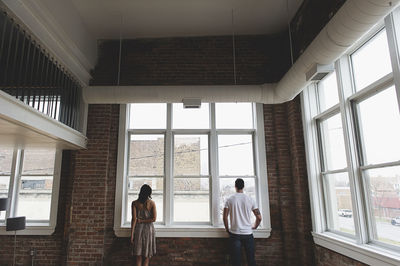 Rear view of couple looking through window while standing at home