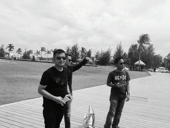 Friends standing on floorboard against cloudy sky