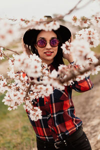 Portrait of woman wearing sunglasses and hat amidst pink flowers