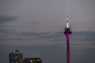 Communications tower in city against sky at sunset