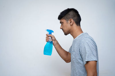 Side view of young man drinking against wall