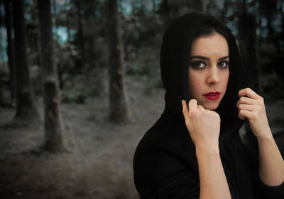 Portrait of young woman wearing black hooded jacket in forest