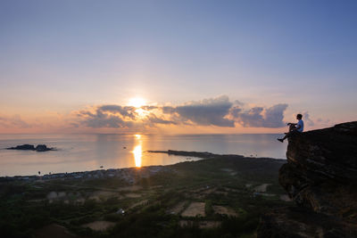 Man standing on rock against sky during sunset