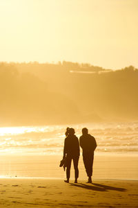 Silhouette friends walking against sea during sunset