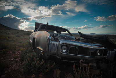 Abandoned car on landscape against sky