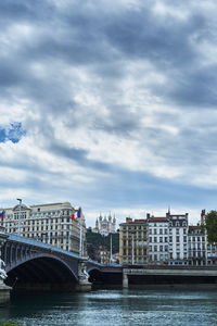 Bridge over river by buildings against sky