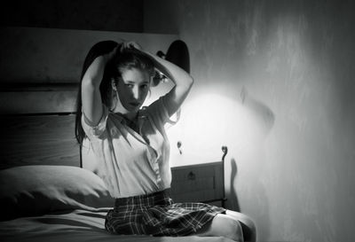 Woman holding hair while sitting on bed at home