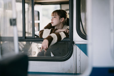 Portrait of young woman looking through window