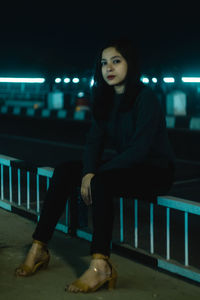 Portrait of young woman sitting on railing at night