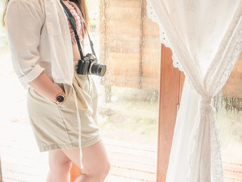 Midsection of woman holding umbrella standing by window