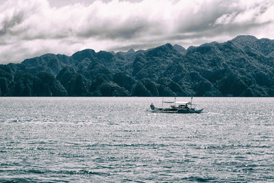 Boat sailing on sea against mountains