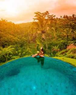 A girl sitting on the edge of a pool in the middle on jungle in bali, indonesia