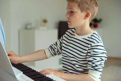 Midsection of boy playing piano at home