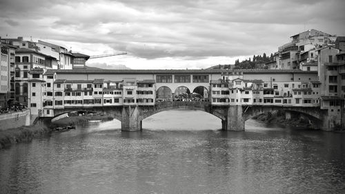 Bridge over river by buildings against sky