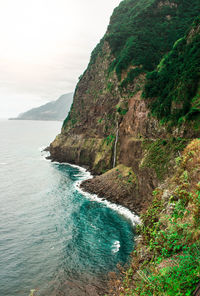 Scenic view of sea by mountain against sky