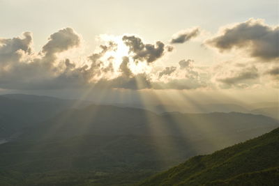 Sunlight streaming through clouds over landscape