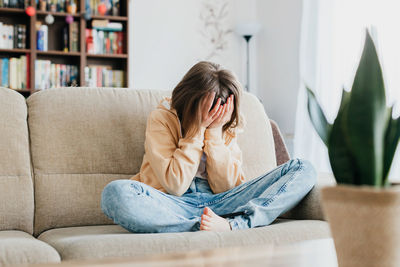 Tired schoolgirl girl sits on the couch and holds on with her hands. per head. children's stress 