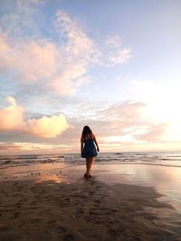 Rear view of woman on beach against sky during sunset