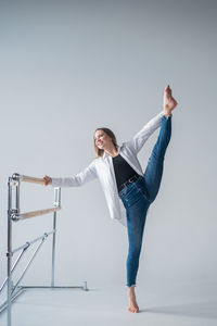 Caucasian woman in casual clothes pulls the split at the ballet barre. 