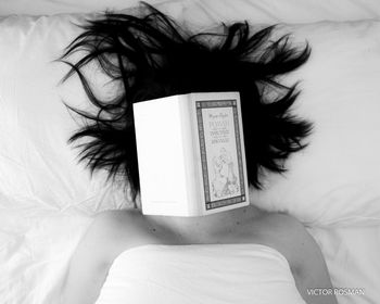 High angle view of woman reading book on bed