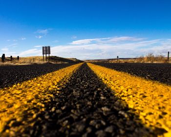 Surface level of asphalt road against blue sky on sunny day