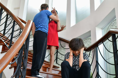 Tensed boy sitting on steps with angry couple in background