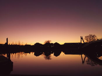 Scenic view of lake by silhouette house against sky during sunset