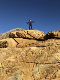 Low angle view of man standing with arms outstretched on mountain against sky