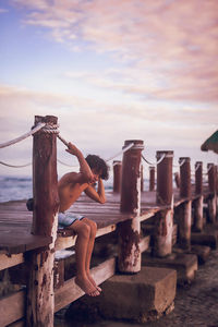 Full length of woman relaxing on wood against sea