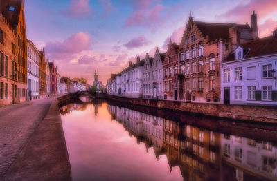 Canal amidst buildings in city against sky at sunset