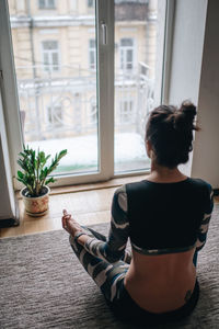 Rear view of woman sitting on window