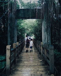 Rear view of father and son walking on footbridge in forest