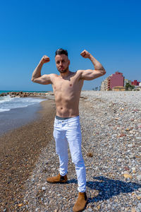 Full length of shirtless man standing on shore at beach