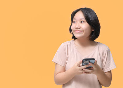 Young woman using smart phone while standing against yellow background