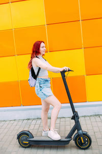 Young bright woman smiles and rides an electric scooter in the summer in city