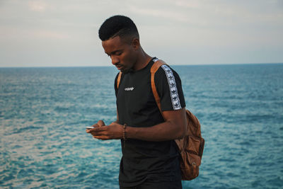 Young man standing in sea against sky