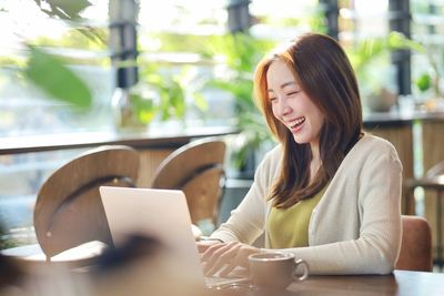 Young woman using mobile phone while sitting on table