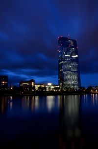 Illuminated buildings by river against sky at night