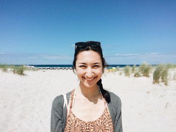 Portrait of happy woman standing at sandy beach against blue sky on sunny day