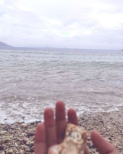 Midsection of person on sea shore against sky