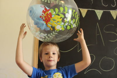 Portrait of cute boy holding ball against blackboard
