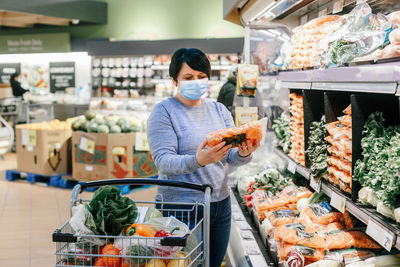 Grocery shopping. middle age woman with short dark hair in protective face mask choosing buying food