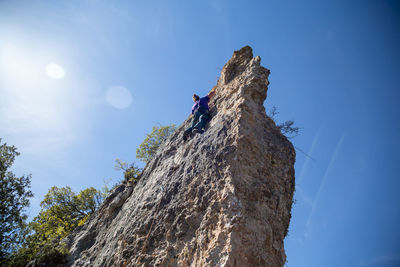 Low angle view of man climbing on rock formation against sky during sunny day