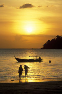 Silhouette people on beach against sky during sunset