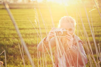 Young woman photographing grass with camera during sunset