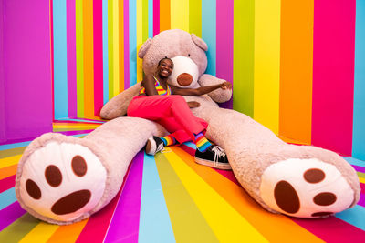 Young woman sitting on giant teddy bear against colored background