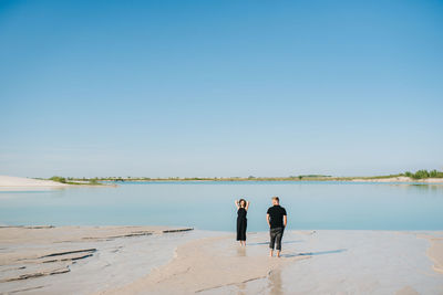 Rear view of friends standing on shore against sky