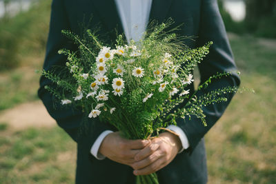 Midsection of bridegroom holding flowers while standing outdoors