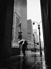 Full length of man with umbrella while walking on sidewalk during rainy season